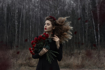 Russia, Moscow - 11/14/2020: A beautiful girl with curly blond hair stands in a black dress with flowers.