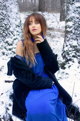 Beautiful girl in a blue dress and a black fur coat in the forest.