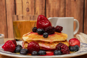 Stack of homemade pancakes prepared with blueberries, strawberries and maple syrup or honey dripping pancakes on an old plate on a wooden table. Concept healthy food at breakfast.