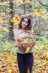 The girl in the autumn forest smiles with a basket of mushrooms in her hands.