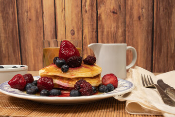 Stack of homemade pancakes prepared with blueberries, strawberries and maple syrup or honey dripping pancakes on an old plate on a wooden table. Concept healthy food at breakfast.