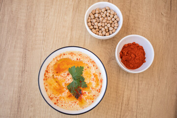 Top view of a Bowl with Hummus typical of the Middle Eastern or Arab food and two containers with chickpeas and paprika with wooden bottom. Concept of typical ethnic food.