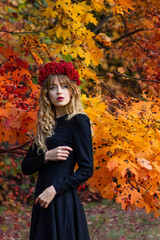 Beautiful girl in a black dress in a wreath of mountain ash in the autumn forest.