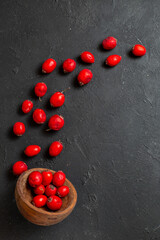 Vertical view of fresh red cornel berries pouring out brown bowl on dark background