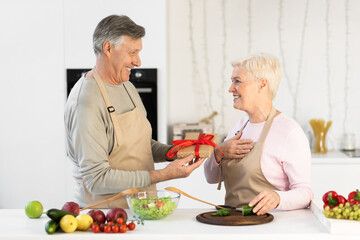 Senior Man Giving Birthday Gift To Wife Standing In Kitchen