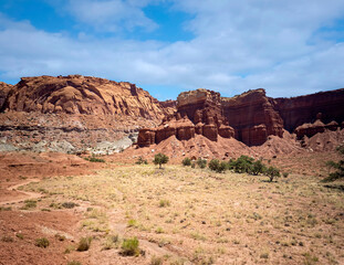 Fototapeta premium Amazing sandstone monoliths in a barren desert prairie on a blue partly cloudy summer day at Capitol Reef National Park in Torrey Utah