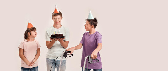 Teenaged disabled boy holding cake while celebrating birthday together with his friends in birthday...