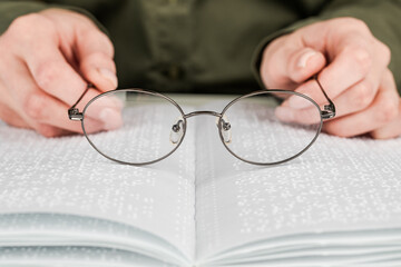 A woman holds black-rimmed glasses against the background of an open textbook reading books in Braille