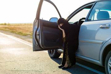 Muslim woman sitting in broken car empty road.