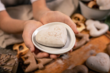 Girl hands hold heart shaped gingerbread. Wooden planks Christmas background