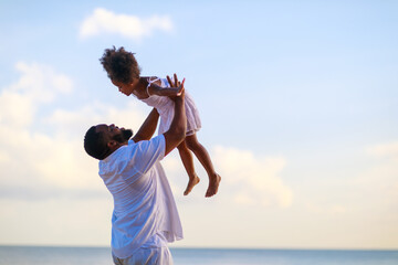 Smiling African american father carrying little daughter on beach during holiday time.