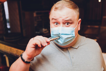 a man without clothes in a medical mask lights a pod e-cigarette through a mask, copy space, close...