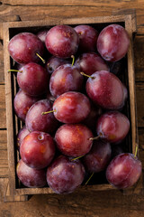 Fresh plums in crate on rustic wooden table. Top view. Close up