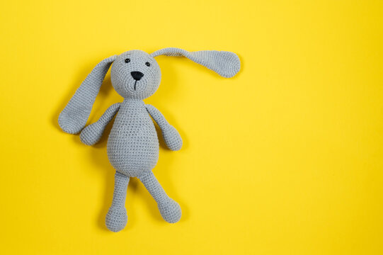 Grey knitted toy rabbit on yellow background with copy space. Top view