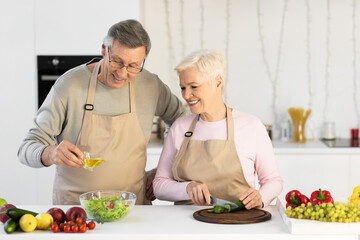 Happy Senior Couple Making Salad Together In Kitchen At Home