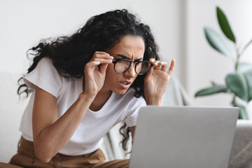 Young woman with bad eyesight using laptop, wearing glasses - obrazy, fototapety, plakaty