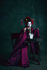 Delicious food. Young japanese woman as geisha isolated on dark green background. Retro style, comparison of eras concept. Beautiful female model like bright historical character, old-fashioned.