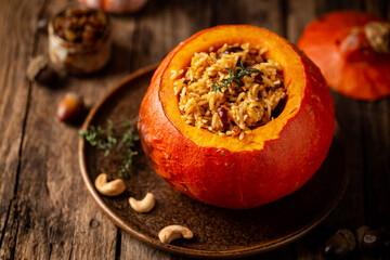 Tasty baked pumpkin stuffed with rice, vegetables, cashews and dried fruits on wooden table with dark background