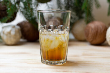 glass of gold rum with ice and cola on wooden table witn christmas tree and balls decoration