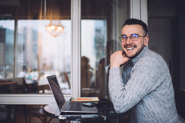 Smiling young man sitting in cafeteria with laptop