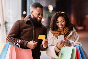Portrait of afro couple using smartphone holding debit credit card