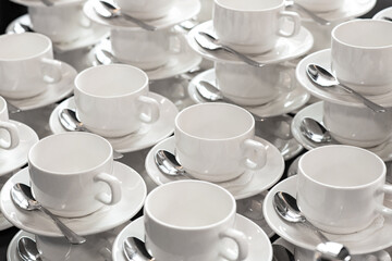 A group of empty white cups and saucers with a teaspoon. Many rows of white cups of tea for serving for breakfast or buffet at the seminar.