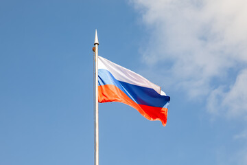 The flag of the Russian Federation flutters in the wind against the blue sky