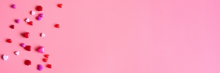 a heap of heart shaped glossy beads in different pink shades on a pink background. banner. space for text