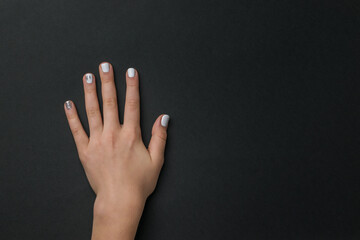 Left hand of a girl with a light manicure on a black background.