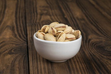 Fried pistachios in a white porcelain cup on a wooden table.