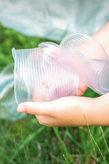 Child's hands clean the park from used plastic utensils in the grass