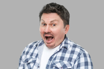 Fototapeta premium Closeup portrait of surprised handsome middle aged business man with mustache in casual checkered shirt standing with amazed face, looking at camera. indoor studio shot, isolated on gray background.