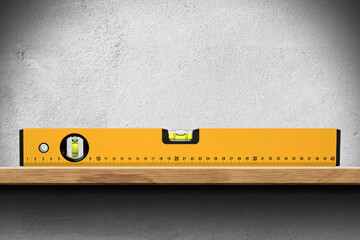 Closeup of an orange bubble level or spirit level on a wooden shelf on white wall. © Alberto Masnovo
