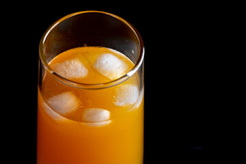 A glass of orange juice with ice cube close-up on a dark background.
