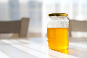 A jar of honey on an old vintage white kitchen table against the sunlight from the window - selective focus