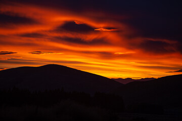 Man taking a picture with a phone of unforgettable red fire sunset in New Zealand at Burke's pass.