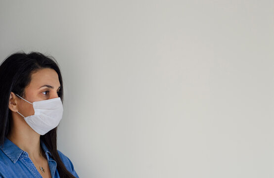 A woman wearing medical mask on a white  blank wall under quarantine at home


