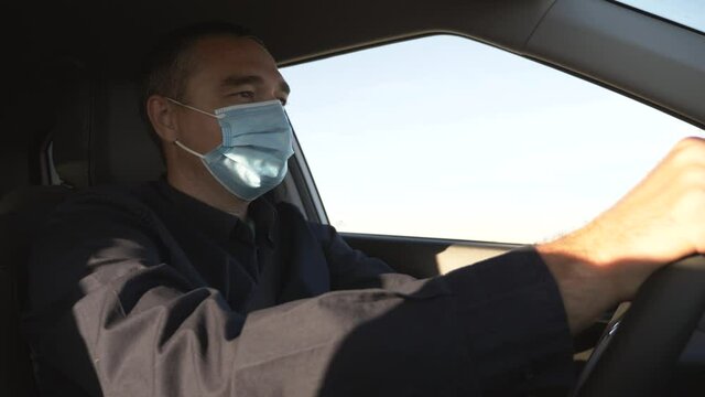 A man driver sits in a car with a protective mask during the coronavirus pandemic. A businessman in a medical mask is driving a car. Traveling by car during a pandemic with protective equipment