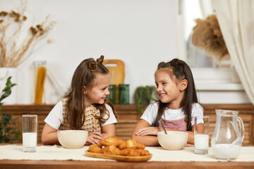 Obraz na płótnie Canvas happy little children girls friends having breakfast - fresh delicious croissants and milk in the kitchen.