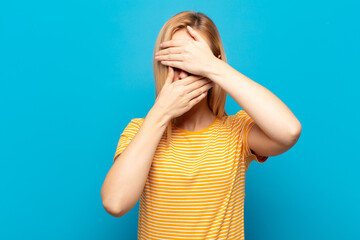 young blonde woman covering face with both hands saying no to the camera! refusing pictures or...