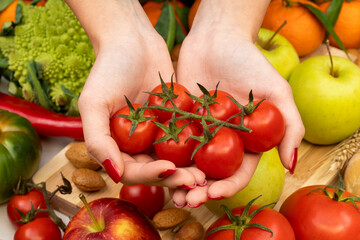 Hands of a girl with red nails holding cherry tomatoes on a table with various types of vegetables