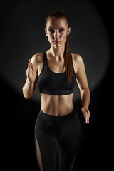 Strong sporty beautiful woman in black sportswear running on dark background. sport and fitness concept