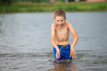 A little boy runs into a cold river. The child swims in the lake in summer.