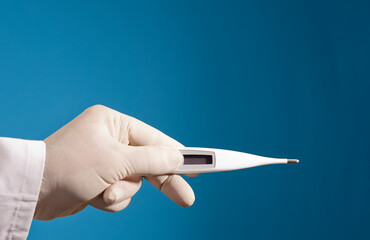 digital thermometer in doctor's hand with surgical glove and blue background.