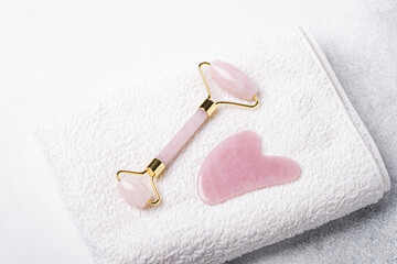 Rose Quartz jade roller and Gua Sha massager on white towel. Massage tool for facial skin care, SPA beauty treatment concept - 399571534