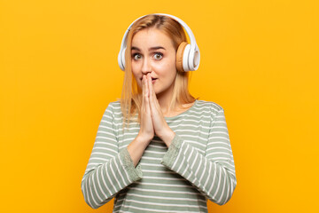 young blonde woman happy and excited, surprised and amazed covering mouth with hands, giggling with...