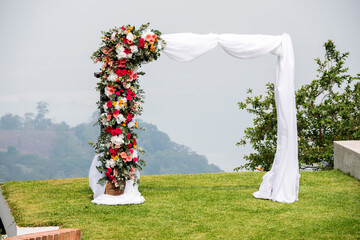 Arch decorated with flowers and white fabric for taking pictures in outdoor ceremony, outdoor wedding decoration.