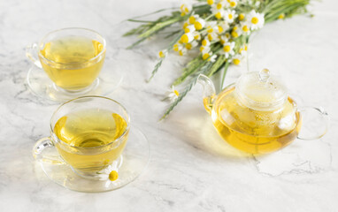 glass cups and teapot with chamomile tea on a white background. a bouquet of daisies.