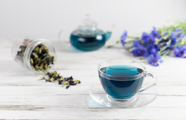 Obraz na płótnie Canvas glass cups and teapot of Butterfly pea tea. Anchan, clitoria ternatea on a white marble background. with bouquet of blue flowers