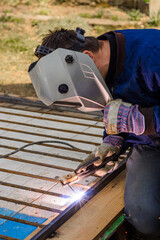 Metal welding, a worker in a protective mask against bright light and sparks, a robot on the street.